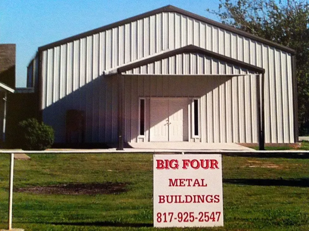 A white metal building with a front porch entrance behind a sign that reads 