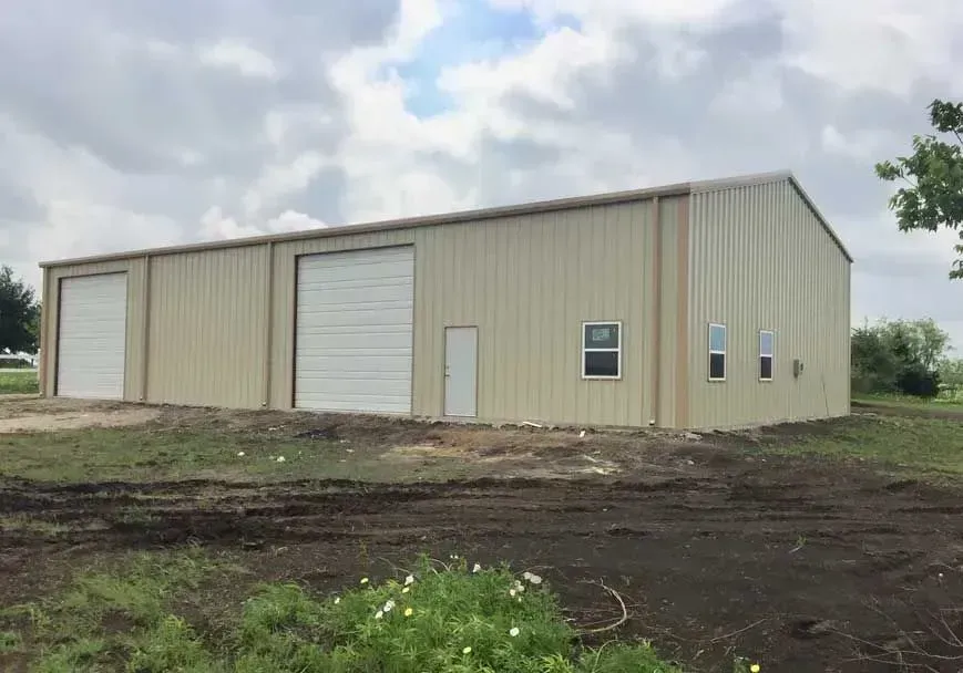 A large, beige metal storage building with two roll-up doors, a single entry door, and three windows on a dirt lot.