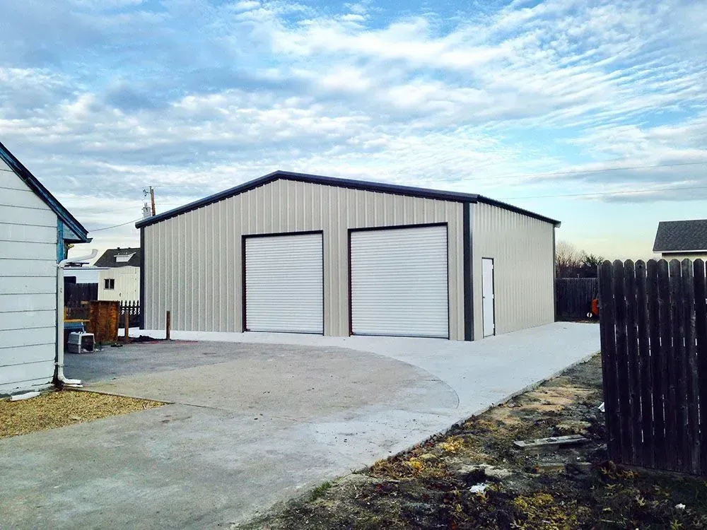 A large, light-colored metal garage building with two roll-up doors and a side entrance, set on a concrete driveway.