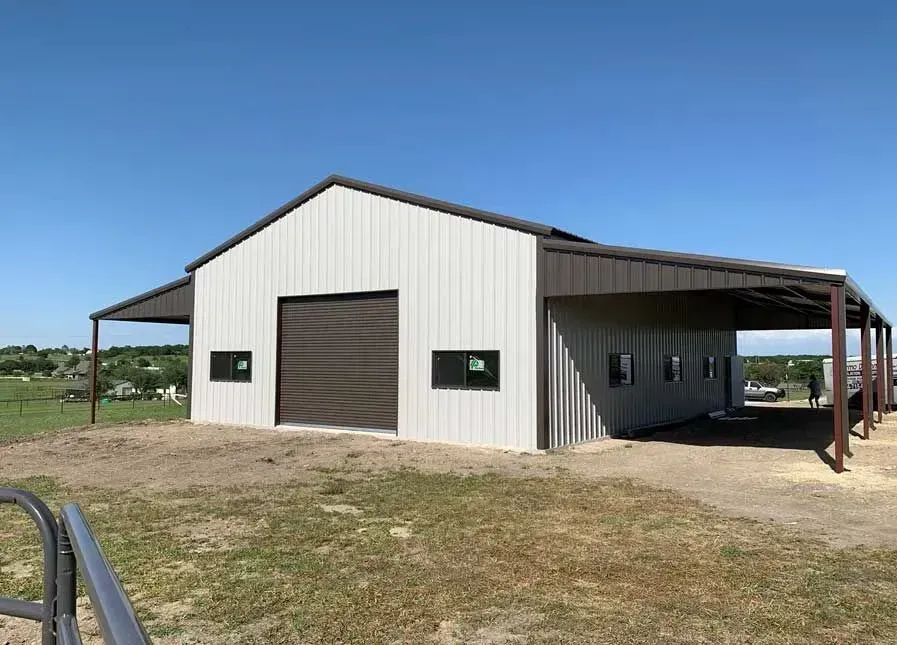 A modern metal barn with white siding, dark trim, a large rolling door, and an open-sided porch in a rural setting.