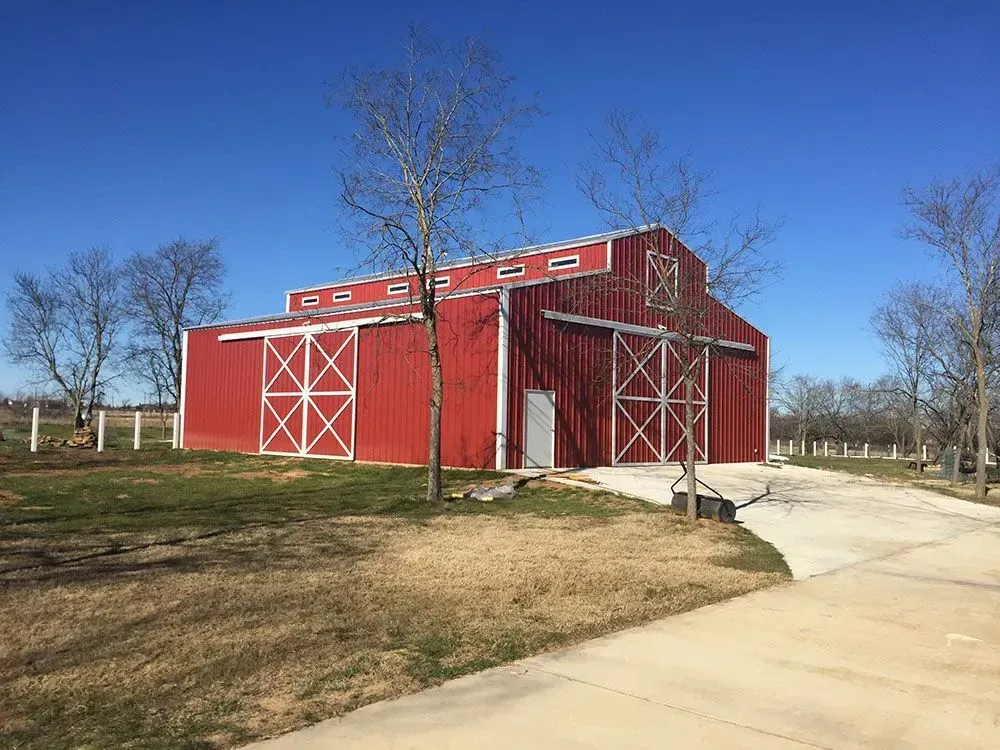 A red barn with white trim and large sliding doors, situated on a grassy lot under a clear blue sky.