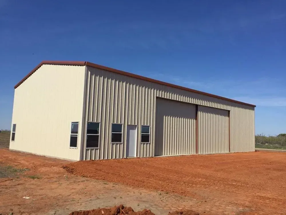 A beige, metal-sided commercial building with a sliding door, single entry door, and windows, set on a red dirt lot.
