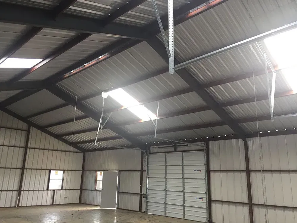 The interior of a large metal warehouse or workshop with visible steel beams, corrugated walls, and skylights.