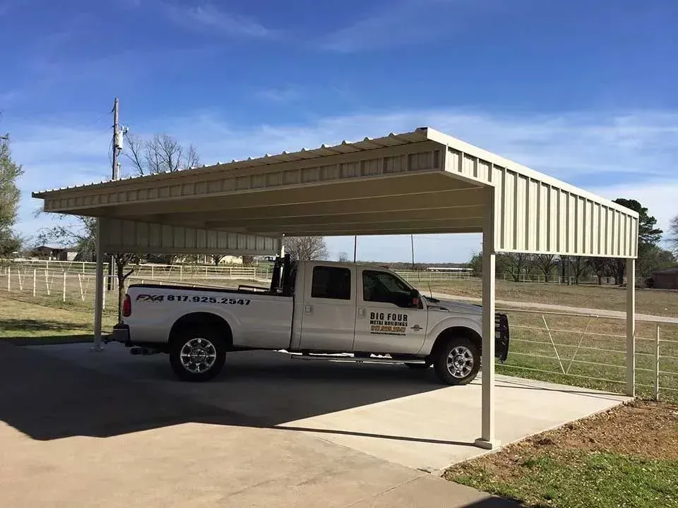 A white pickup truck parked under a tan metal carport structure on a sunny day.