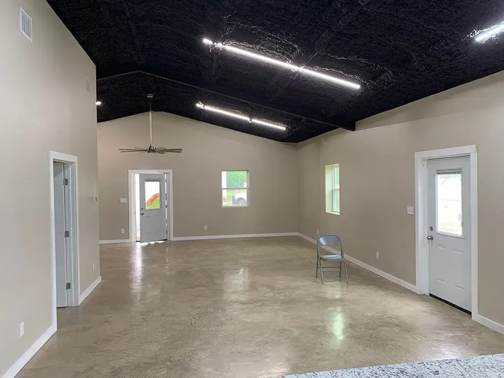 A spacious, modern room with light gray walls, a polished concrete floor, a black vaulted ceiling, and two white doors.