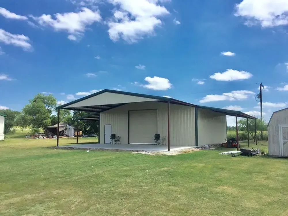 A beige metal building with a large covered porch, central roll-up door, and white entry door on a grassy field.