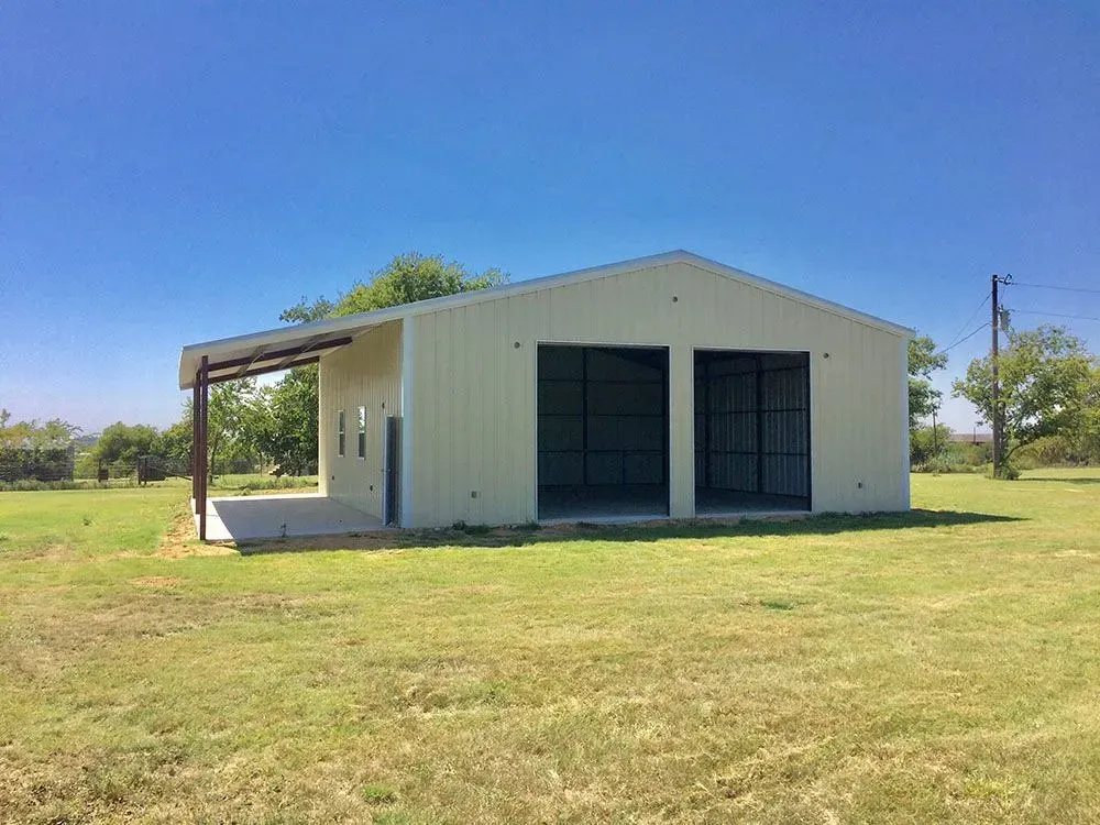A beige metal building with an open-sided porch and two large, empty garage door bays situated on a grassy field.