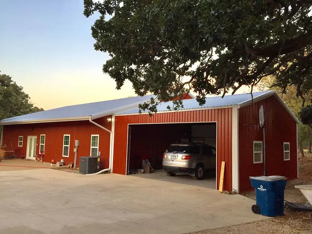 A red metal building with a silver roof, a large garage bay housing a silver SUV, and a concrete driveway.