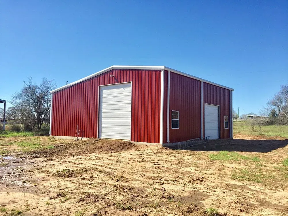 A bright red metal warehouse building with white trim, a large rolling garage door, and a smaller entry door under a sky.