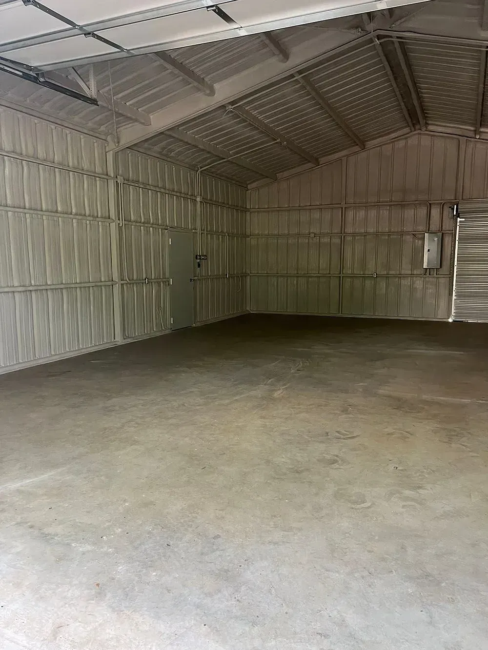 An empty, high-ceilinged workshop or warehouse with concrete floors and walls insulated with silver, textured panels.
