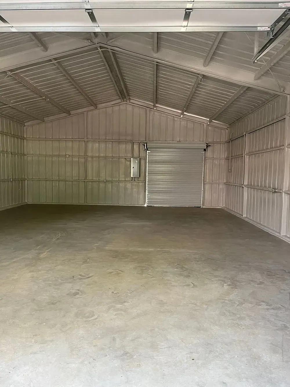 An empty, spacious metal warehouse with light-colored corrugated walls, a concrete floor, and a closed roll-up door.