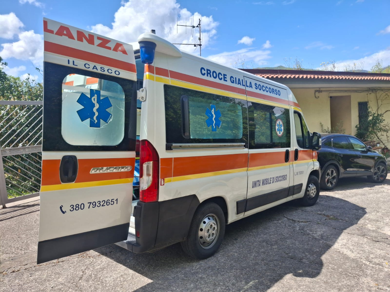 Un'ambulanza con lo sportello posteriore aperto è parcheggiata davanti a un edificio in una giornata di sole.