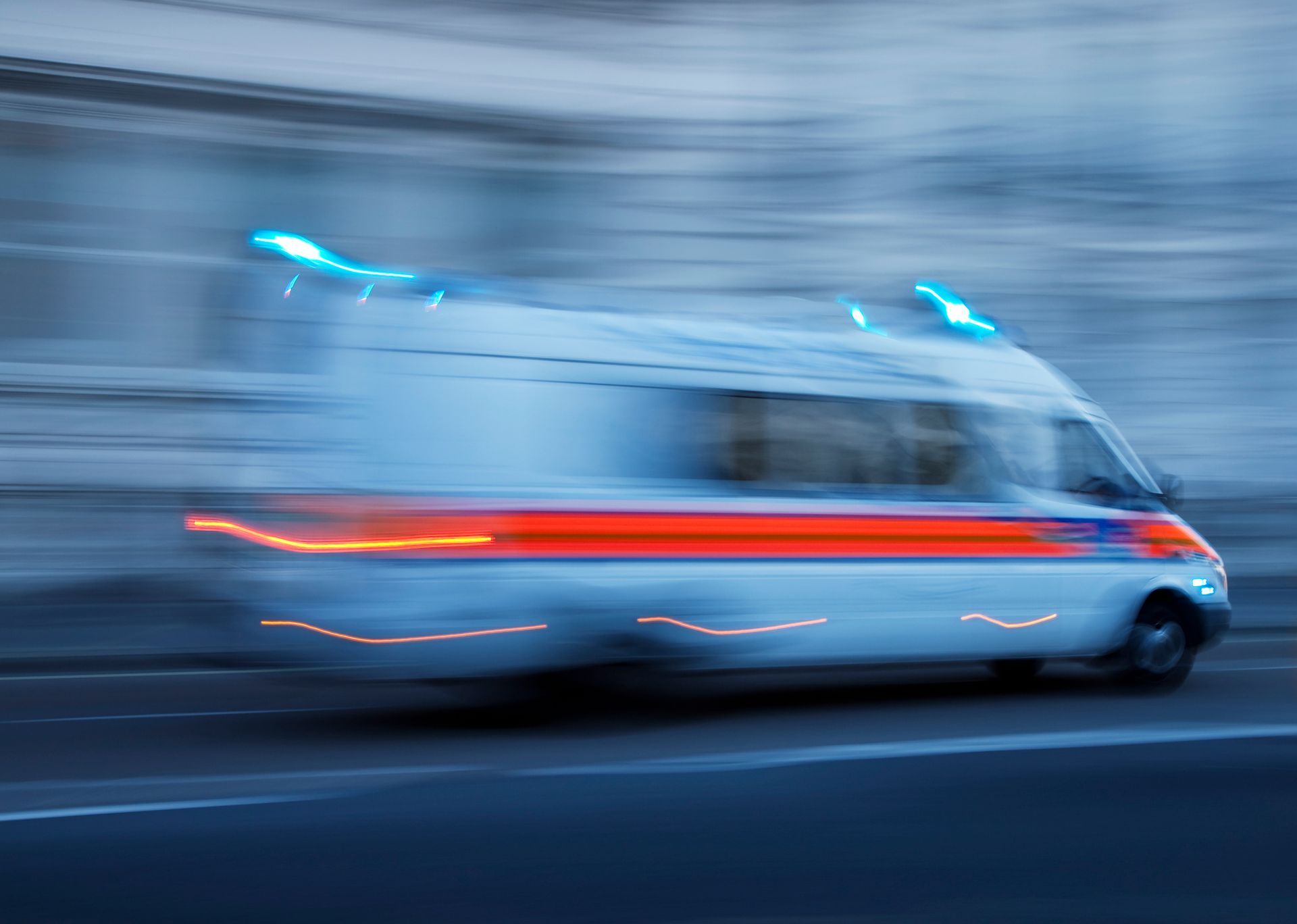 Un'ambulanza bianca sfocata con luci lampeggianti sfreccia su una strada cittadina di notte.
