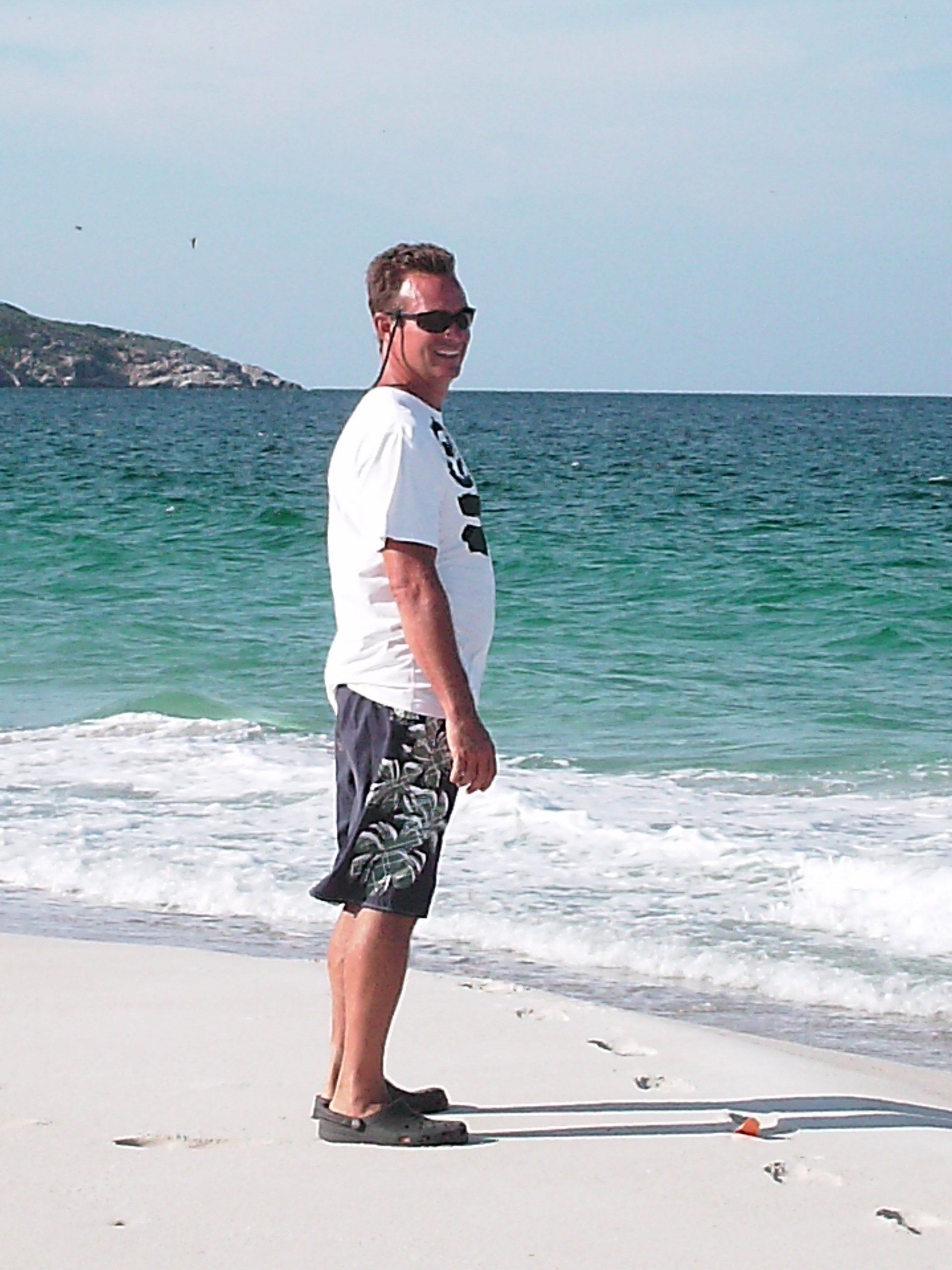 A man is standing on a beach wearing sunglasses