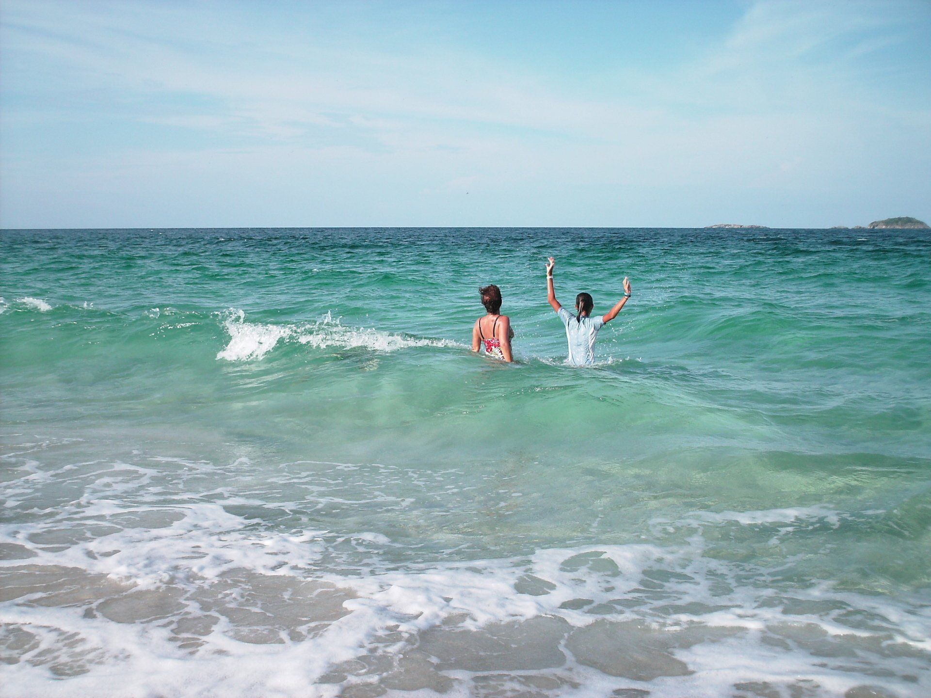 Two people are swimming in the ocean with their arms in the air