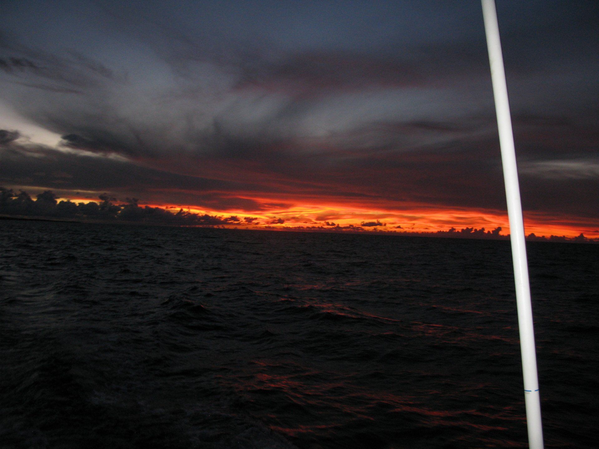 A sunset over a body of water with a white pole in the foreground