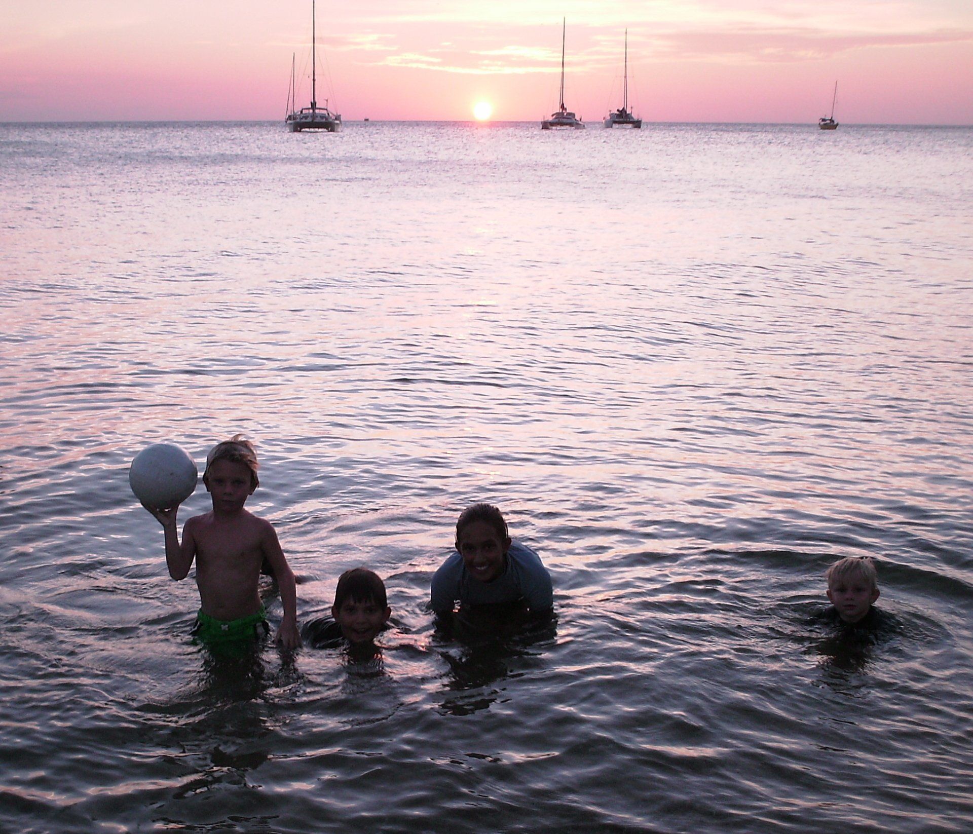 A group of children are playing in the ocean at sunset