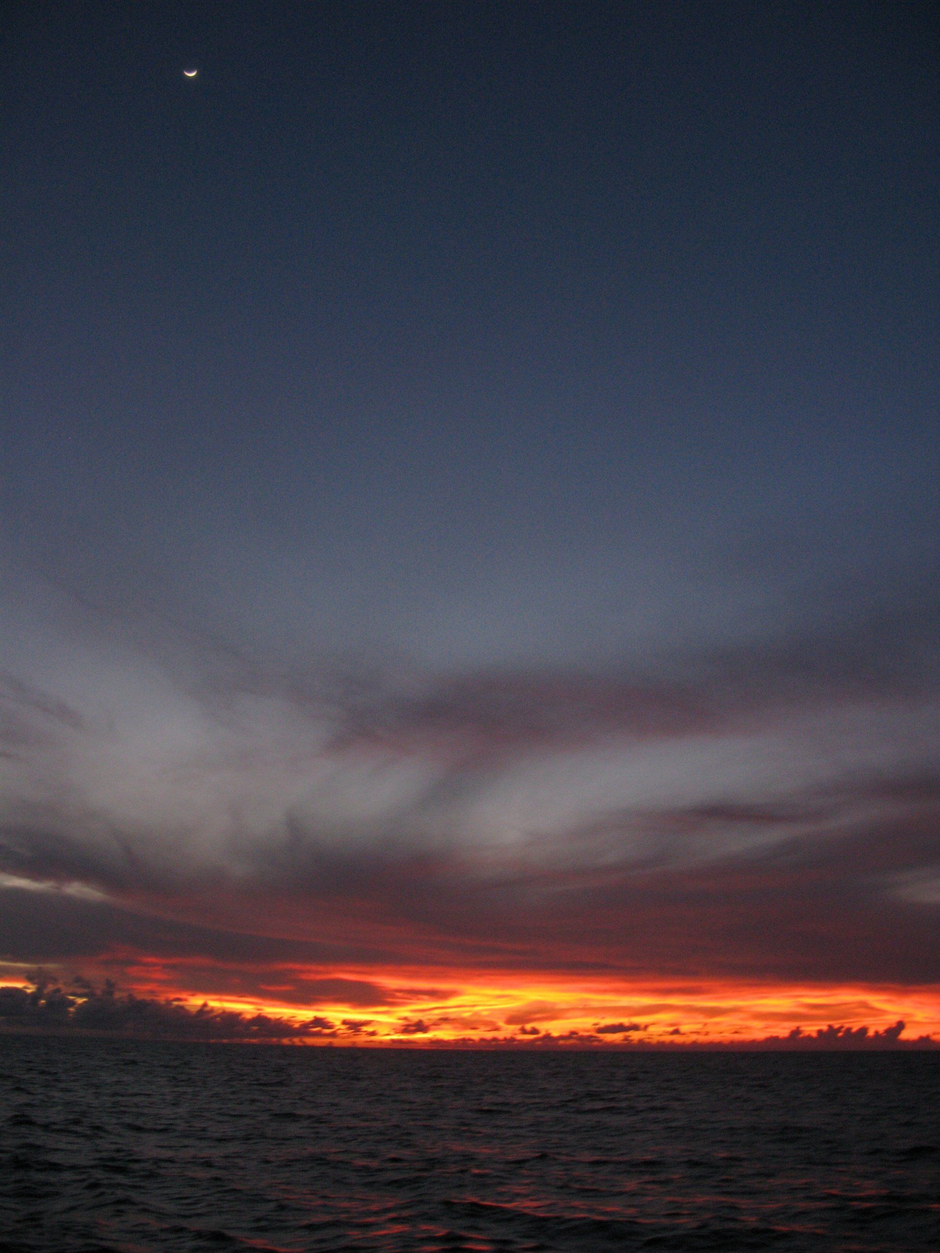 A sunset over the ocean with the moon in the sky