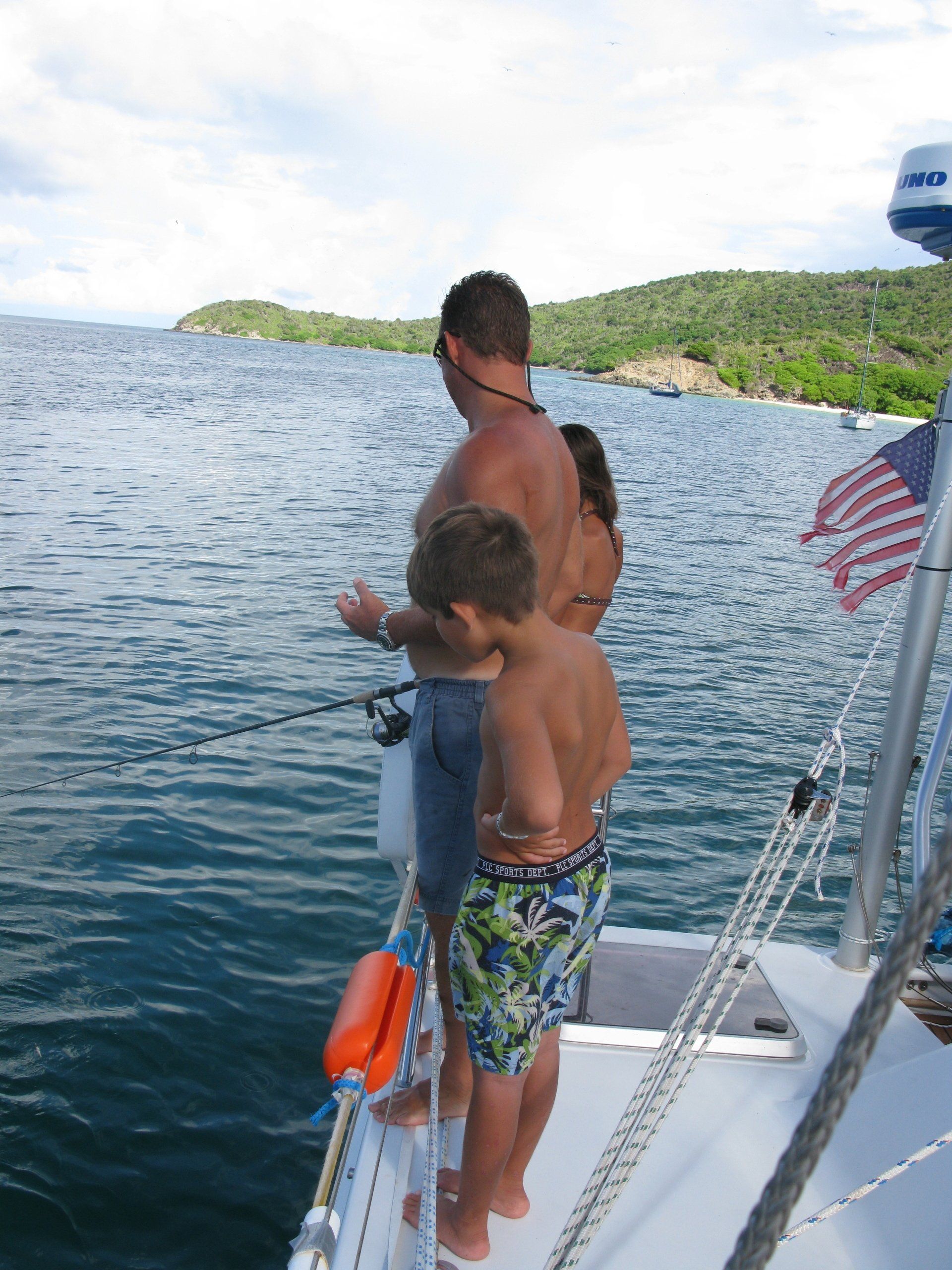 A man and a boy fishing on a boat with an american flag in the background