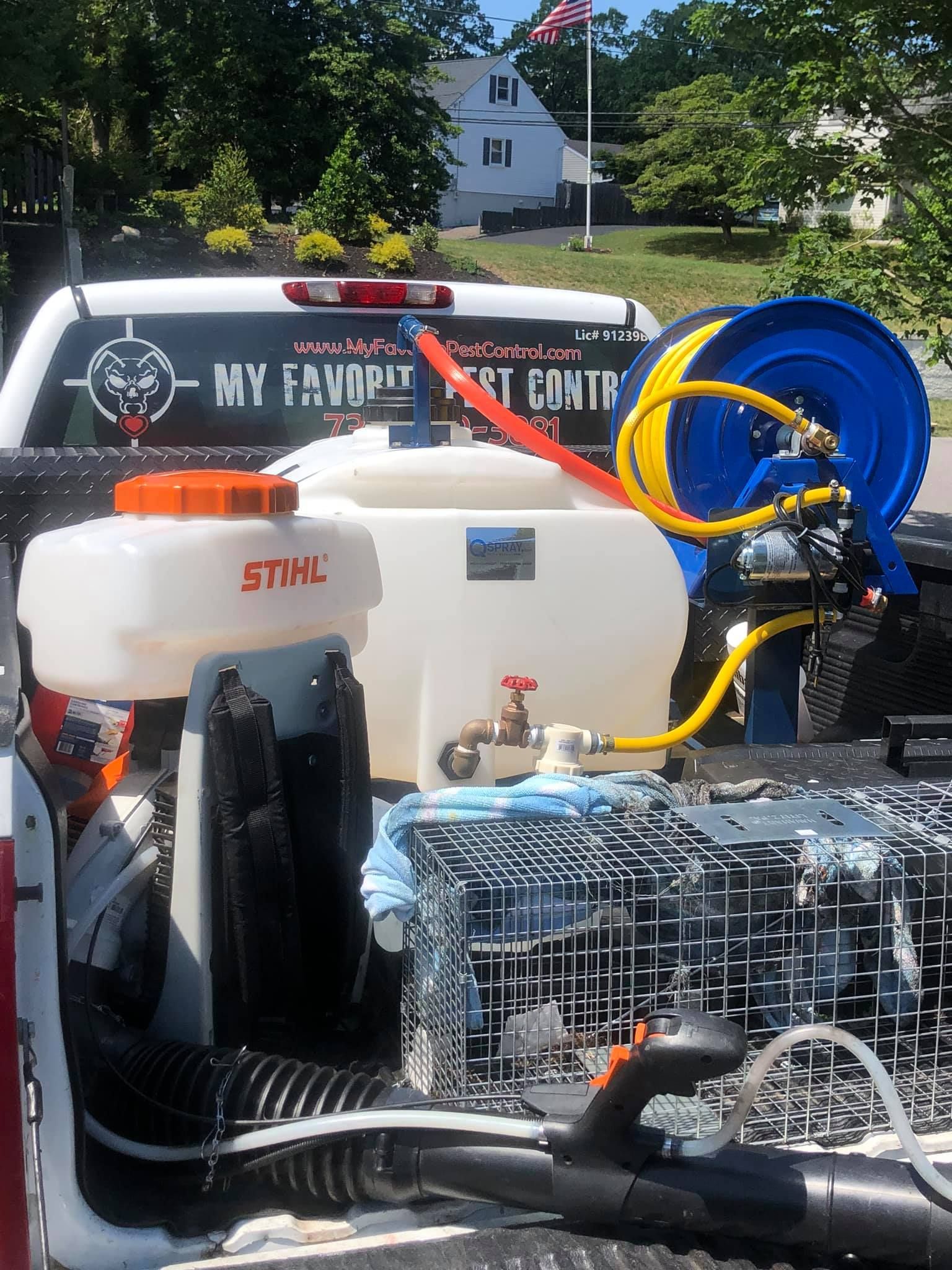 A white truck bed with pest control equipment, including spray tanks, hoses, and a cage, is parked outdoors.