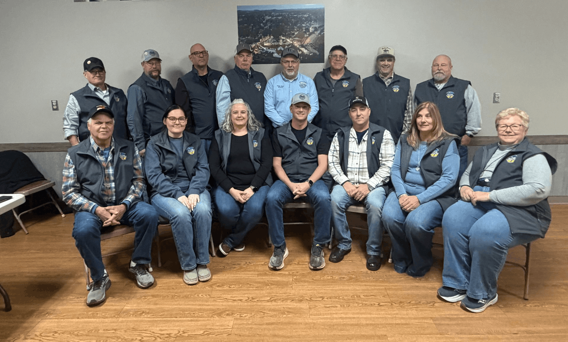 Group of people seated and standing in a meeting room, posing for a group photo.