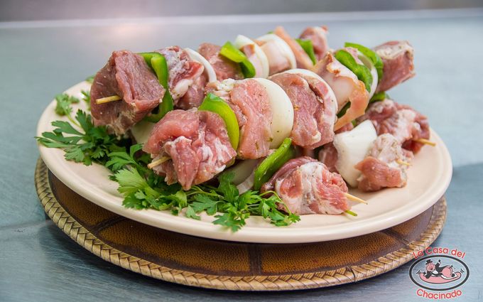 Plato de brochetas de carne cruda con verduras y hierbas sobre un plato blanco.