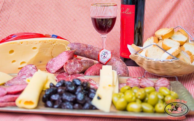 Tabla de embutidos con queso, salami, uvas, pan y una copa de vino tinto.