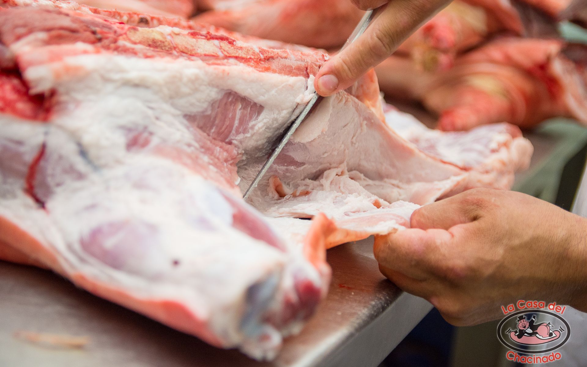 Un carnicero corta la carne en una mesa de acero inoxidable con un cuchillo.