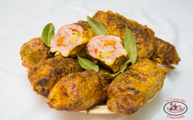 Rollitos de pollo rellenos con especias de cúrcuma y adornados con hojas verdes en un plato blanco.