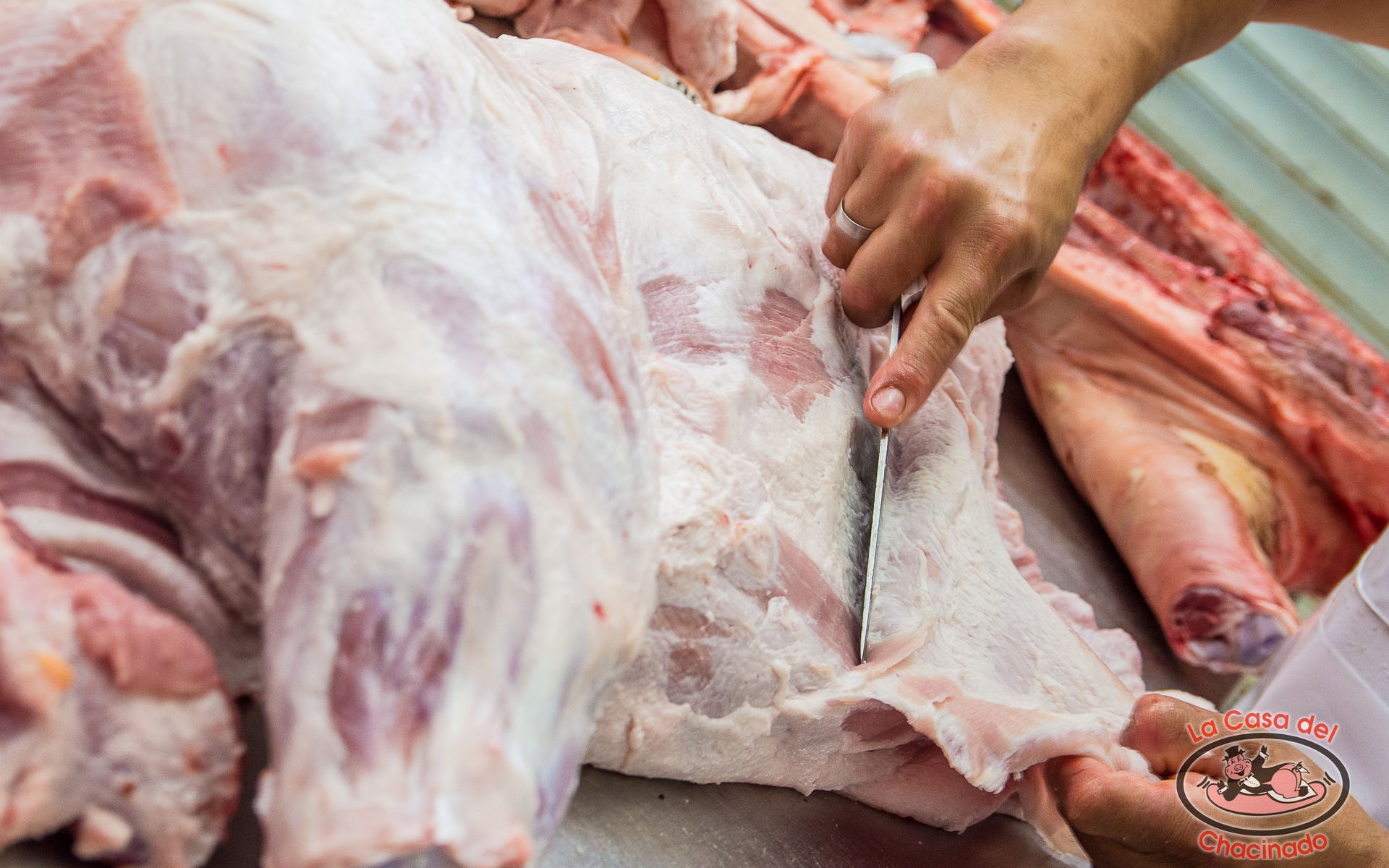 Carne cruda siendo cortada en la mesa de un carnicero por una mano con un cuchillo.