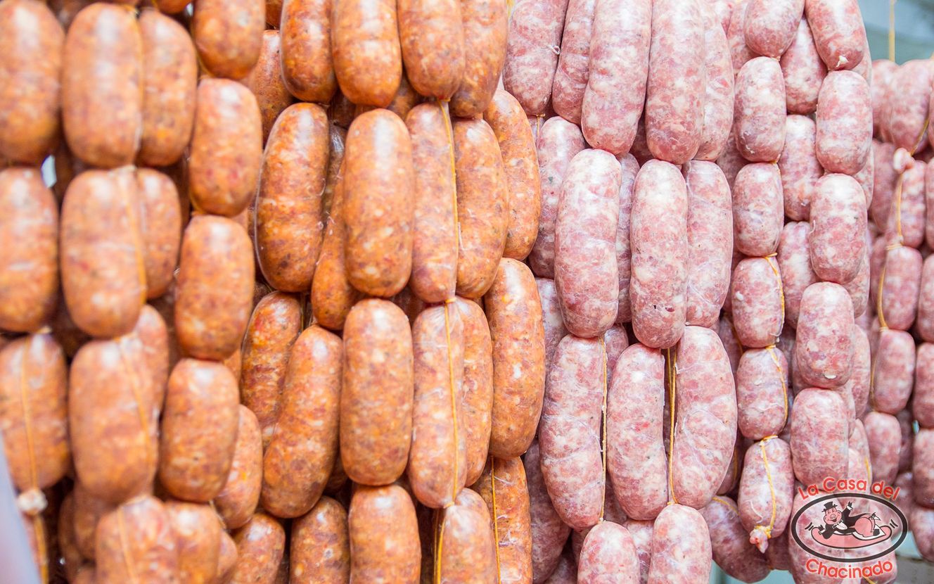 Hileras de salchichas naranjas y rosas colgadas en un puesto del mercado.