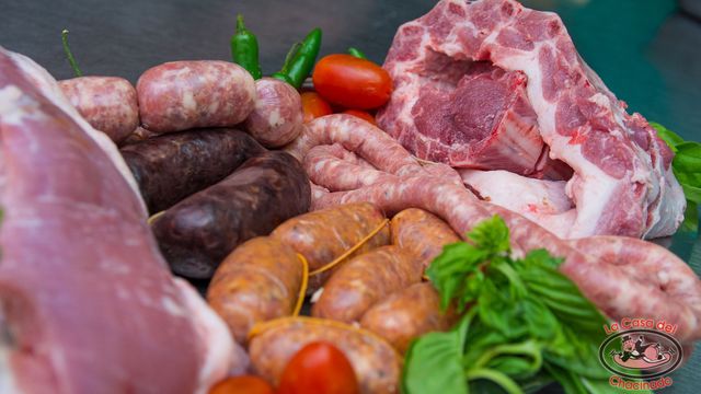 Surtido de salchichas crudas y cortes de cerdo con tomates, pimientos y hierbas en un mostrador de mercado.