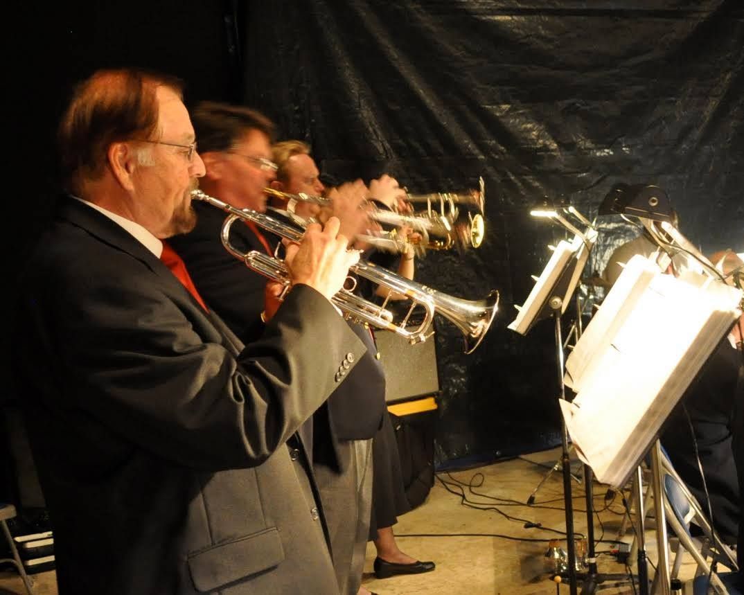 Trumpet players in suits perform on stage, instruments raised.