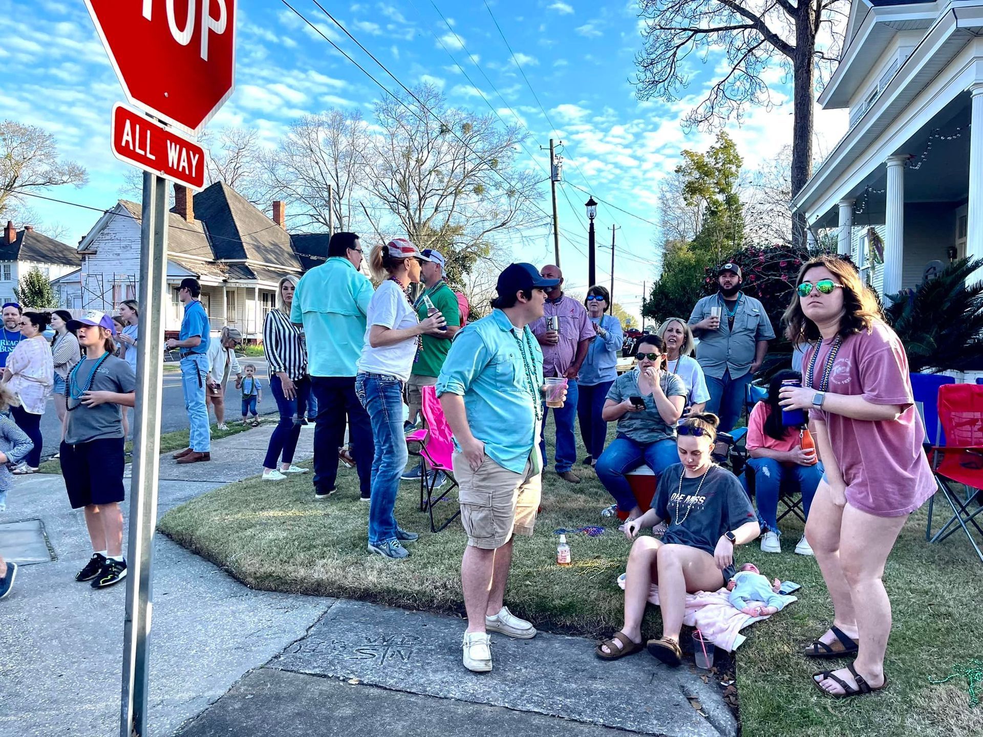 People gathered on a street corner, next to a stop sign, with houses in the background.