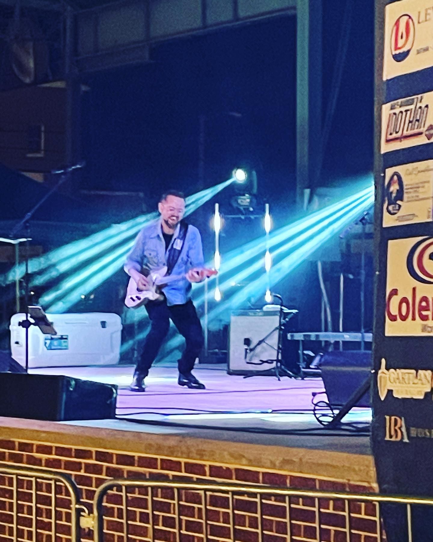 A musician plays an electric guitar on stage, lit by blue spotlights.