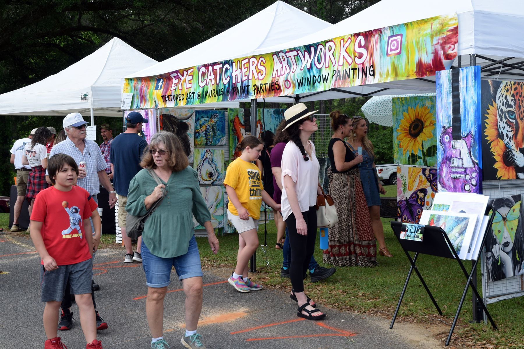 People browsing art at an outdoor festival. Tents with colorful artwork on display.