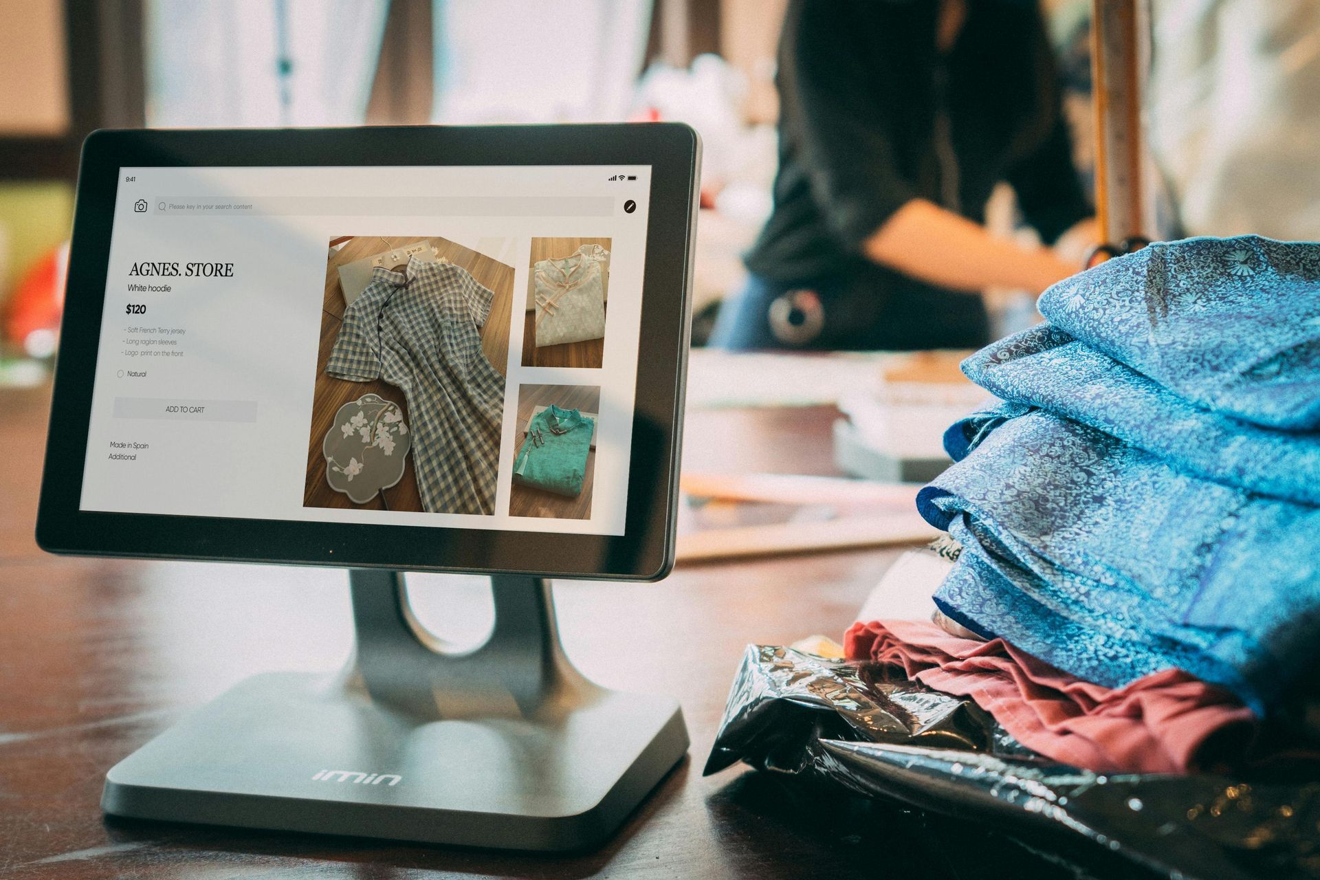 Tablet on a desk showing a clothing website beside folded blue and pink fabrics