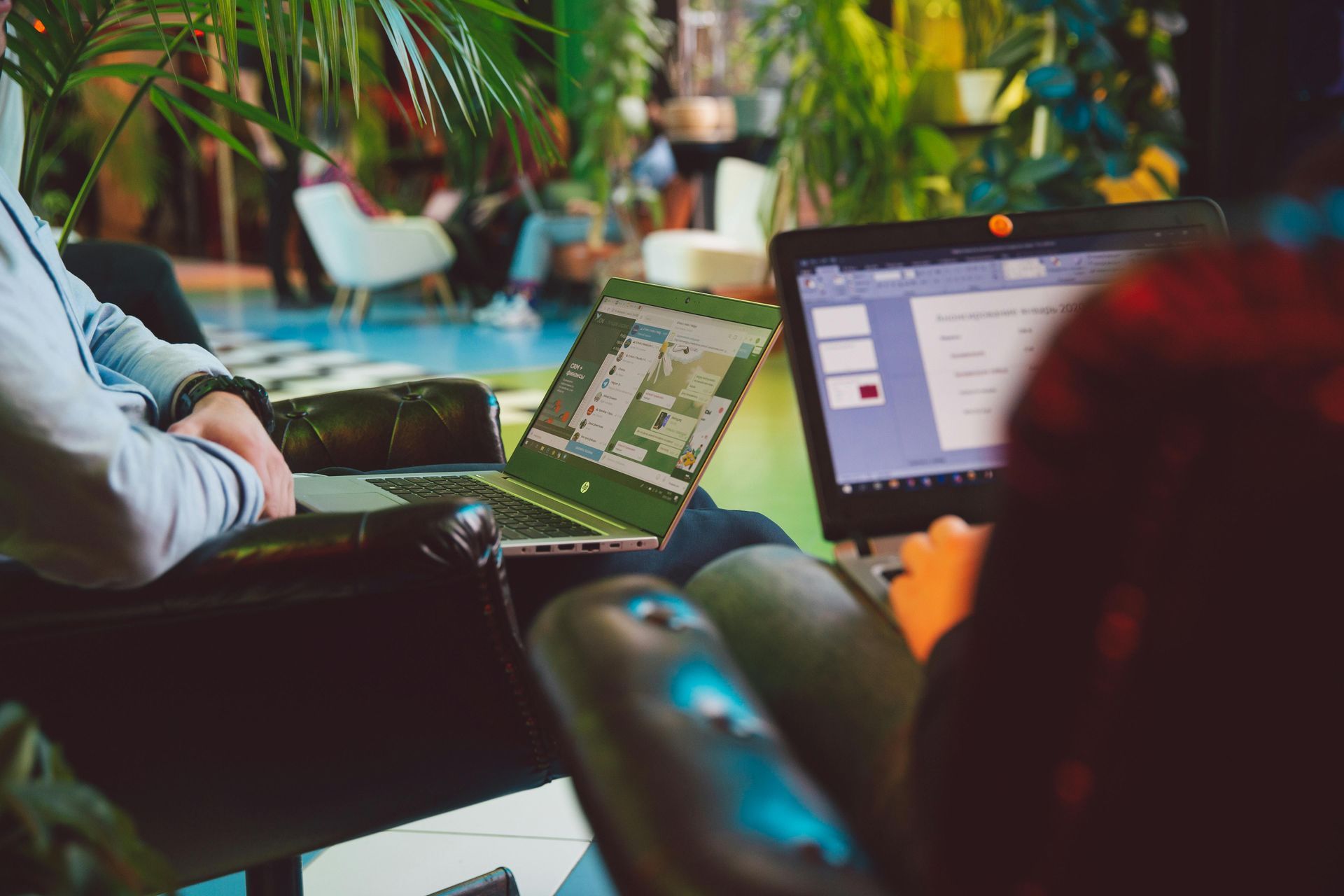People using laptops in a casual indoor workspace, with a blurred colorful background
