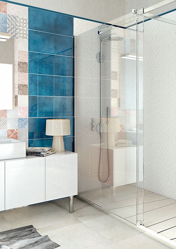Bagno moderno con doccia in vetro, mobile lavabo bianco, parete decorativa con piastrelle blu e pavimento piastrellato beige.