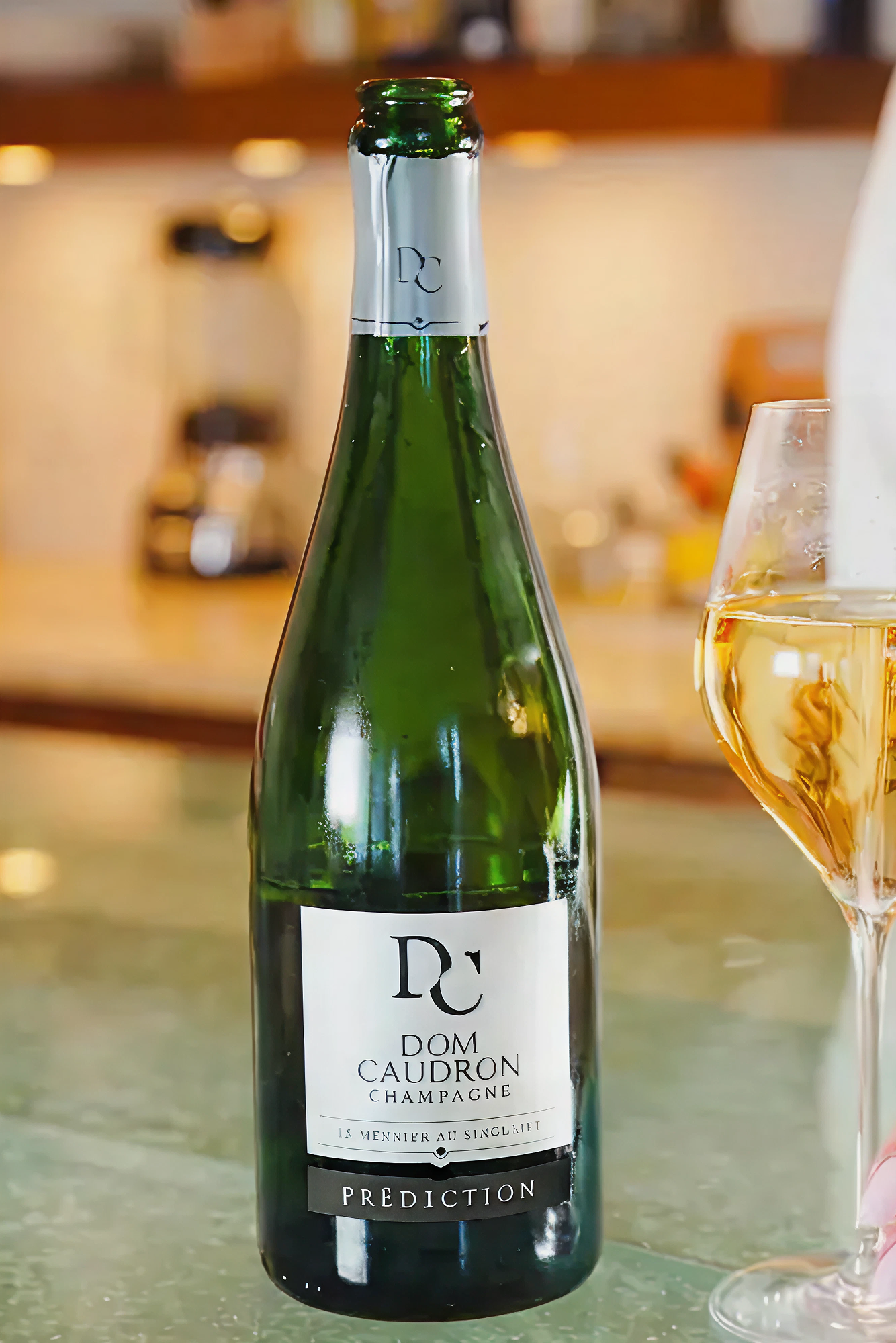 Green champagne bottle with silver foil and label, next to a filled glass.