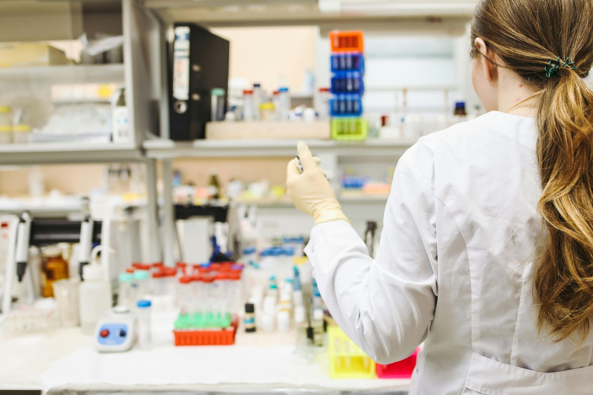 A researcher in a white lab coat uses a pipette while working at a laboratory bench filled with various containers.