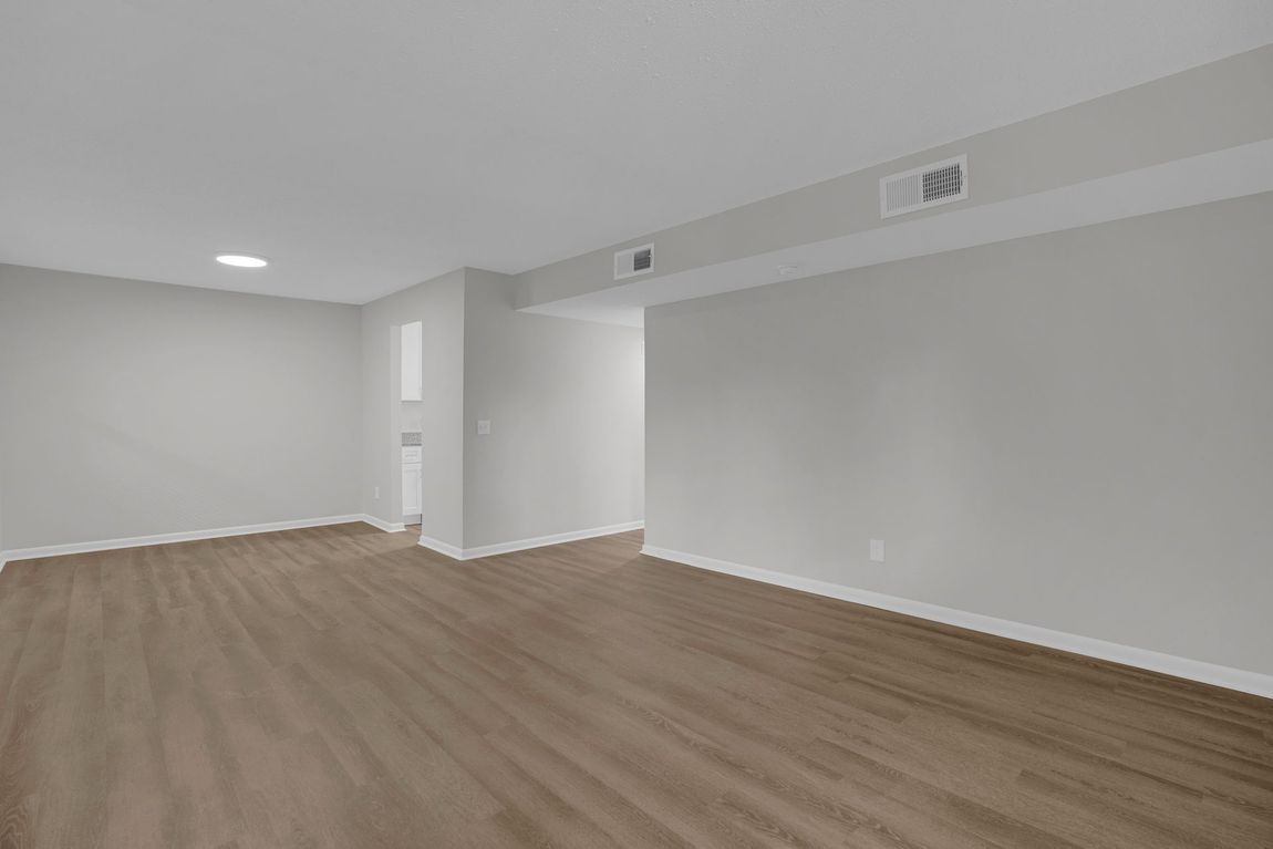An empty room with light gray walls, brown wood-look flooring, and a recessed ceiling area with two air vents.