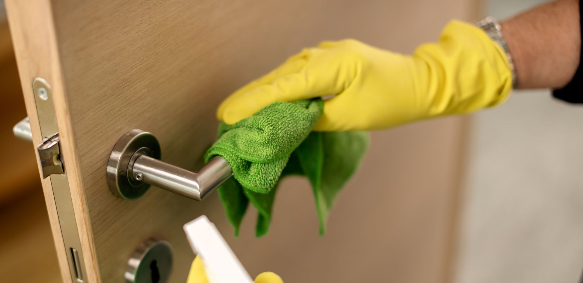 Person wearing blue gloves, cleaning a surface with a spray bottle in an office setting.