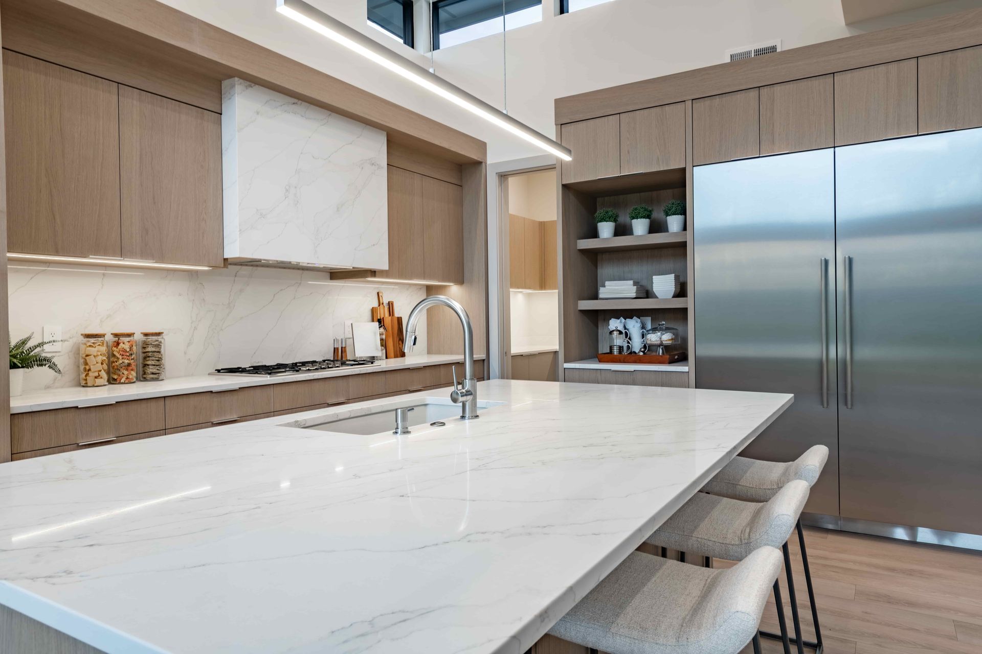 Modern kitchen with a white island, wood cabinets, and stainless steel refrigerator