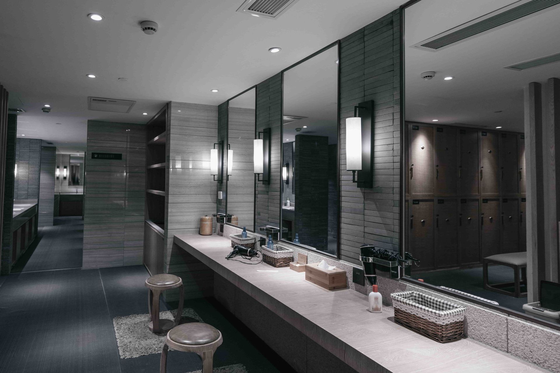 Modern bathroom with long white vanity, large mirror, gray tile walls, and warm lighting