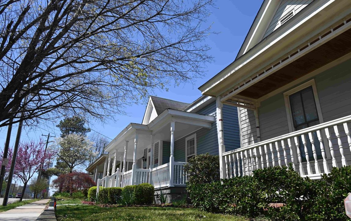 Row of white houses with porches and green hedges along a sunny street