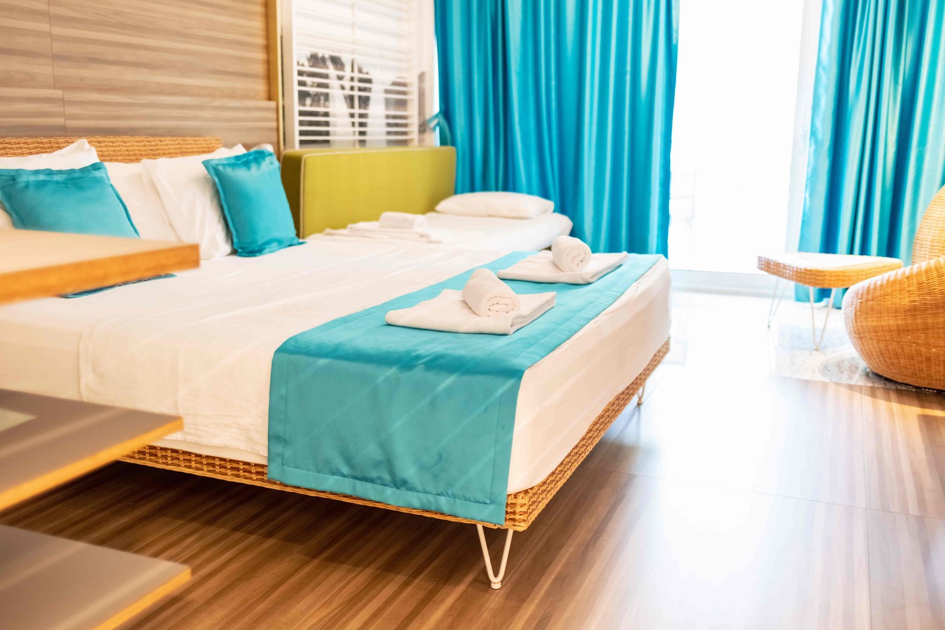 Bright hotel bedroom with turquoise accents, white bed, and a sunlit window with teal curtains