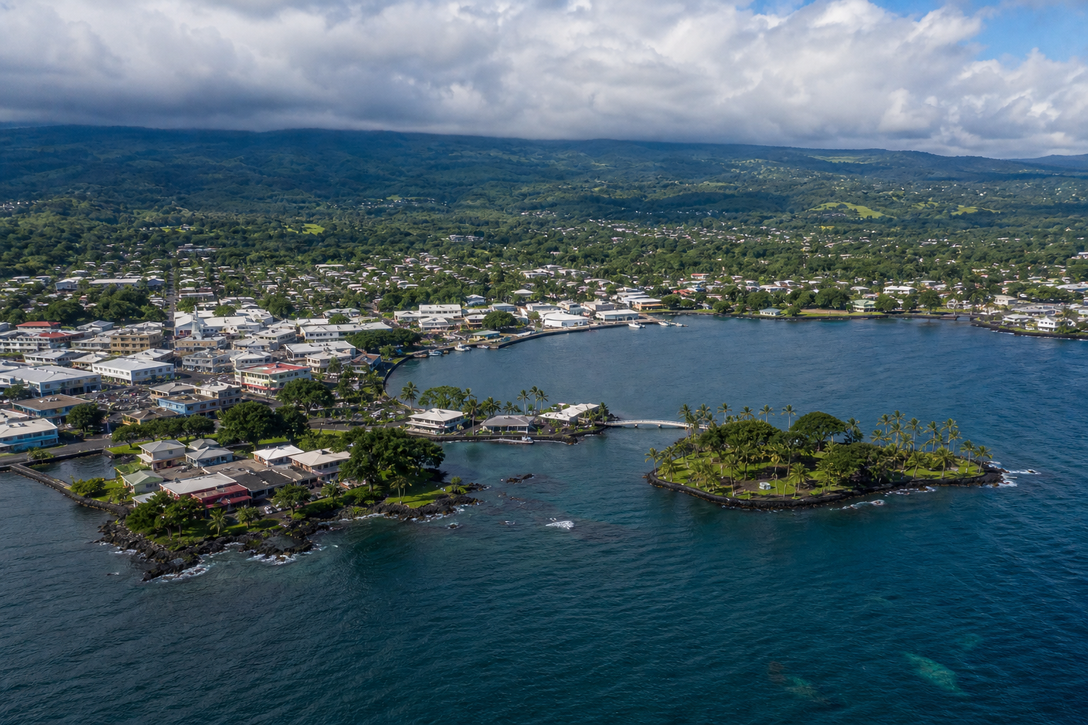 Aerial view of a coastal town with a harbor, blue ocean, and a small green island under cloudy skies