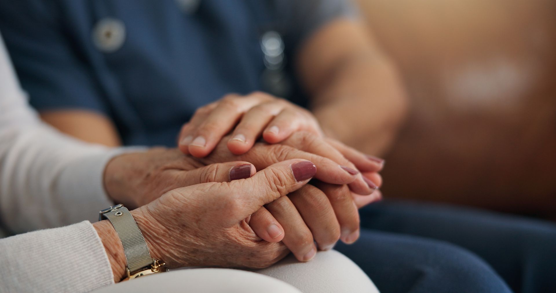 A caregiver’s hands gently hold the hands of another person, showing comfort and support.
