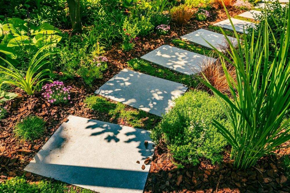 Stepping stones in a garden path surrounded by lush green plants and brown mulch.